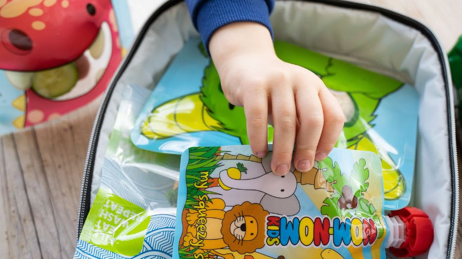 pre-schooler picking up a reusable pouch of yoghurt from his packed lunch at nursery