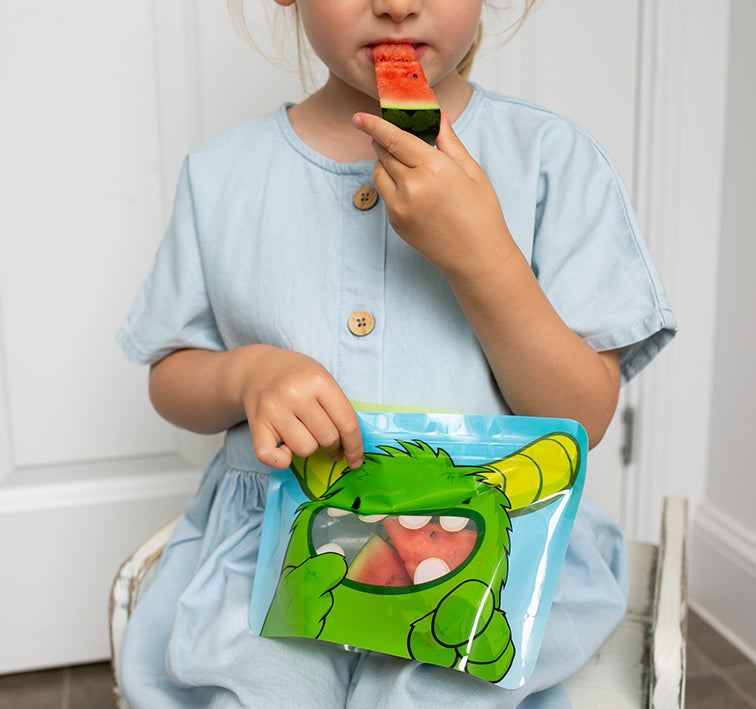 child eating watermelon slice from Nom Nom kids reusable snack pouch.
