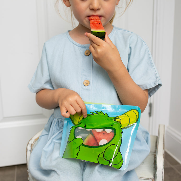 child eating watermelon slice from Nom Nom kids reusable snack pouch.