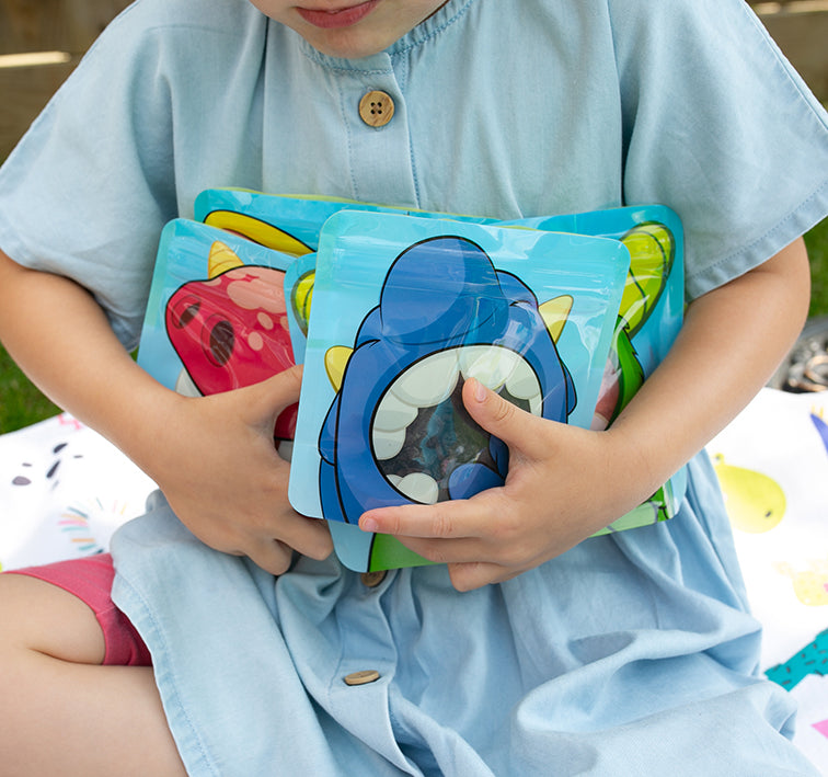 child holding a collection of Nom Nom kids reusable snack bags.