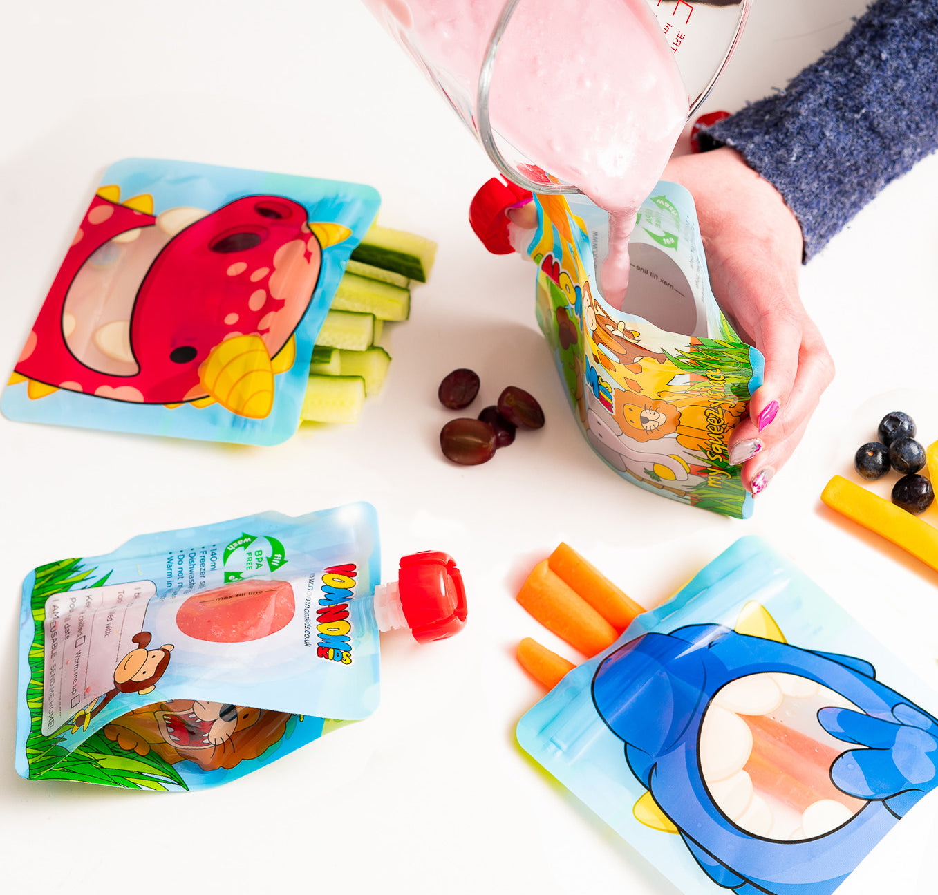 Nom Nom kids reusable snack pouches filled with vegetable sticks and yogurt pouch being filled with homemade smoothie.