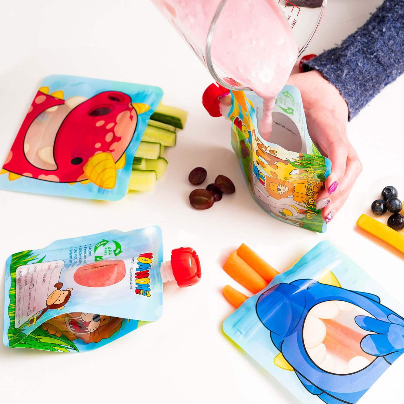 Nom Nom kids reusable snack pouches filled with vegetable sticks and yogurt pouch being filled with homemade smoothie.