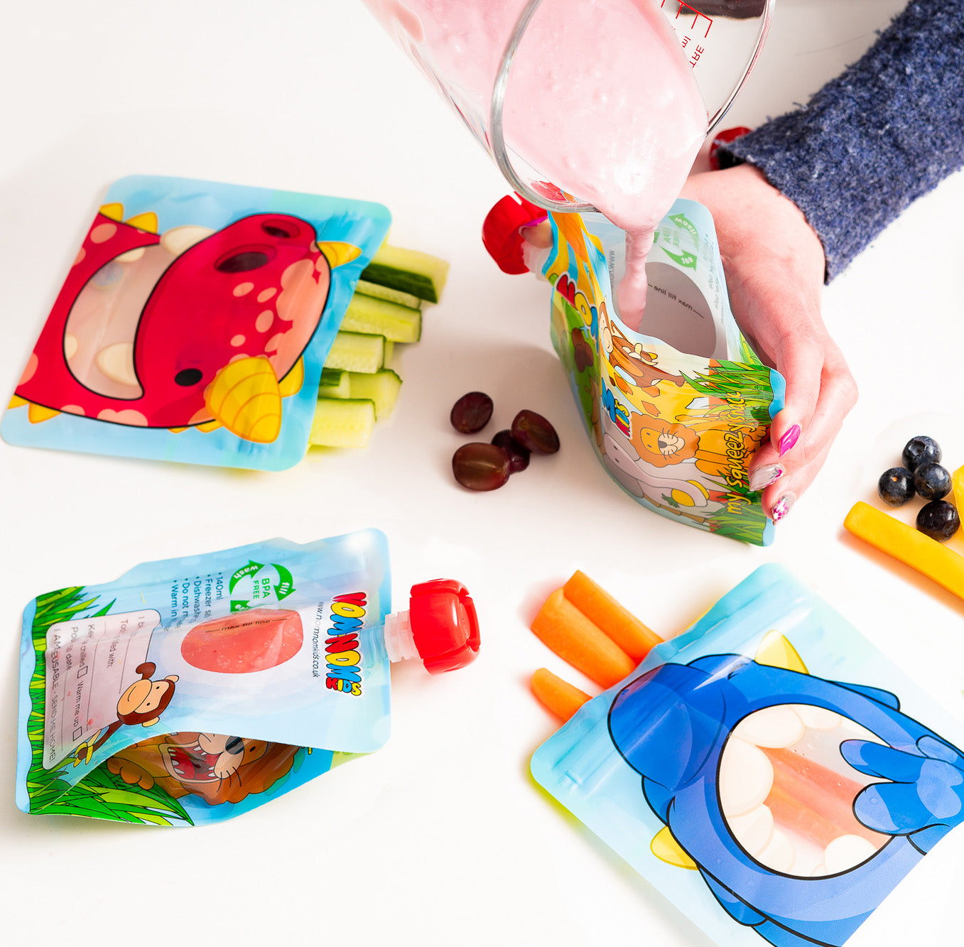 Nom Nom kids reusable snack pouches filled with vegetable sticks and yogurt pouch being filled with homemade smoothie.