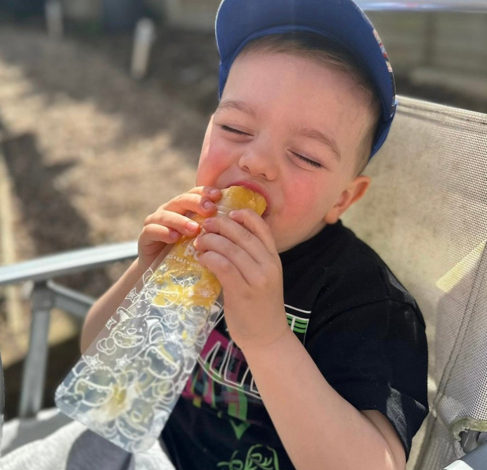 A toddler boy eating an ice pop with his eyes closed and a happy expression