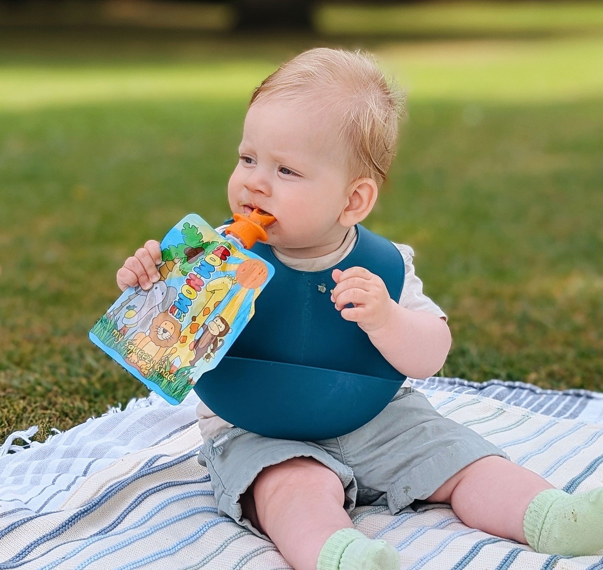 baby outdoors eating from reusable food pouch with silicone pouch spoon attached.