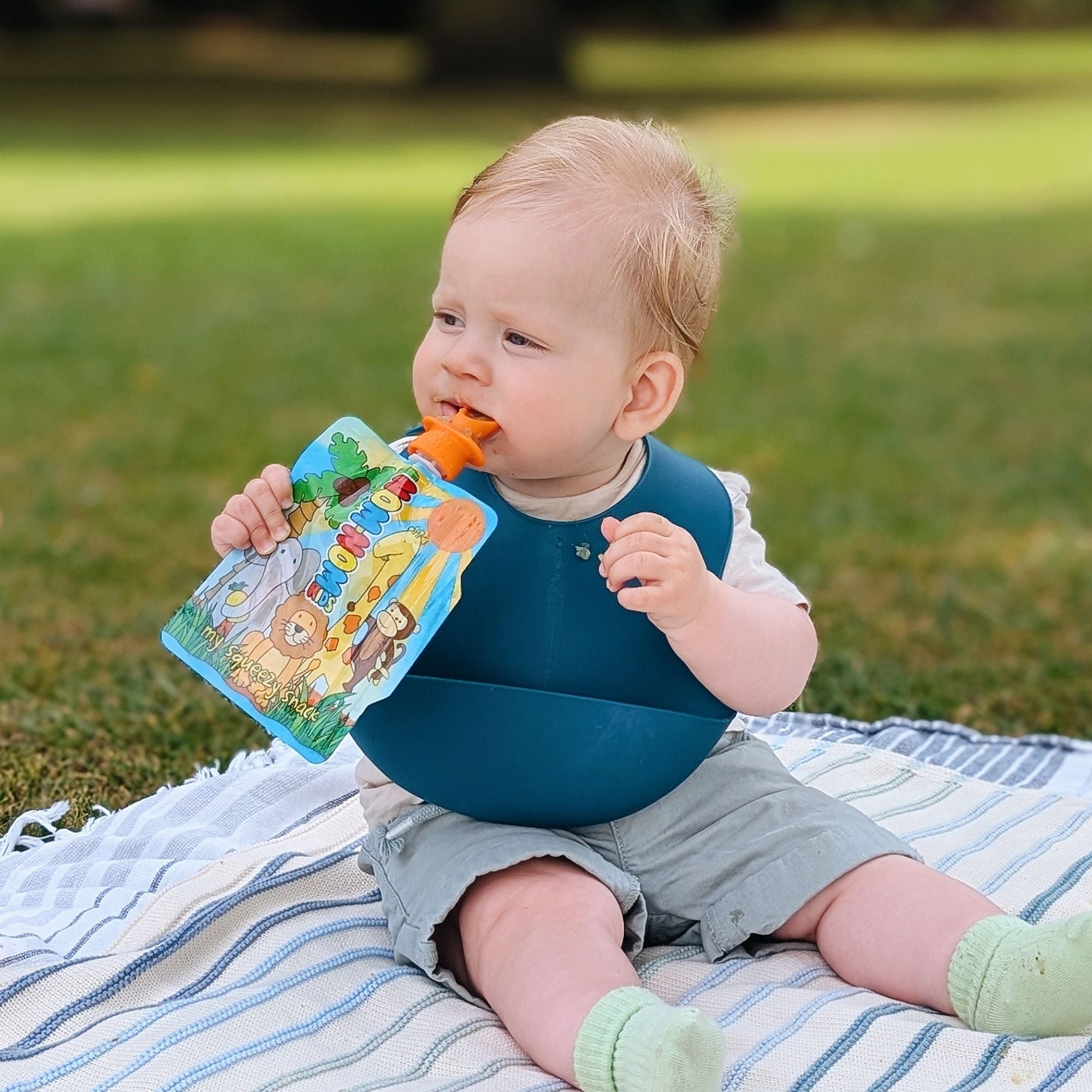 baby outdoors eating from reusable food pouch with silicone pouch spoon attached.