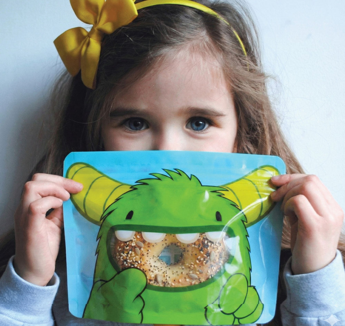 reception age school girl holding a monster bag filled with a seeded bagel