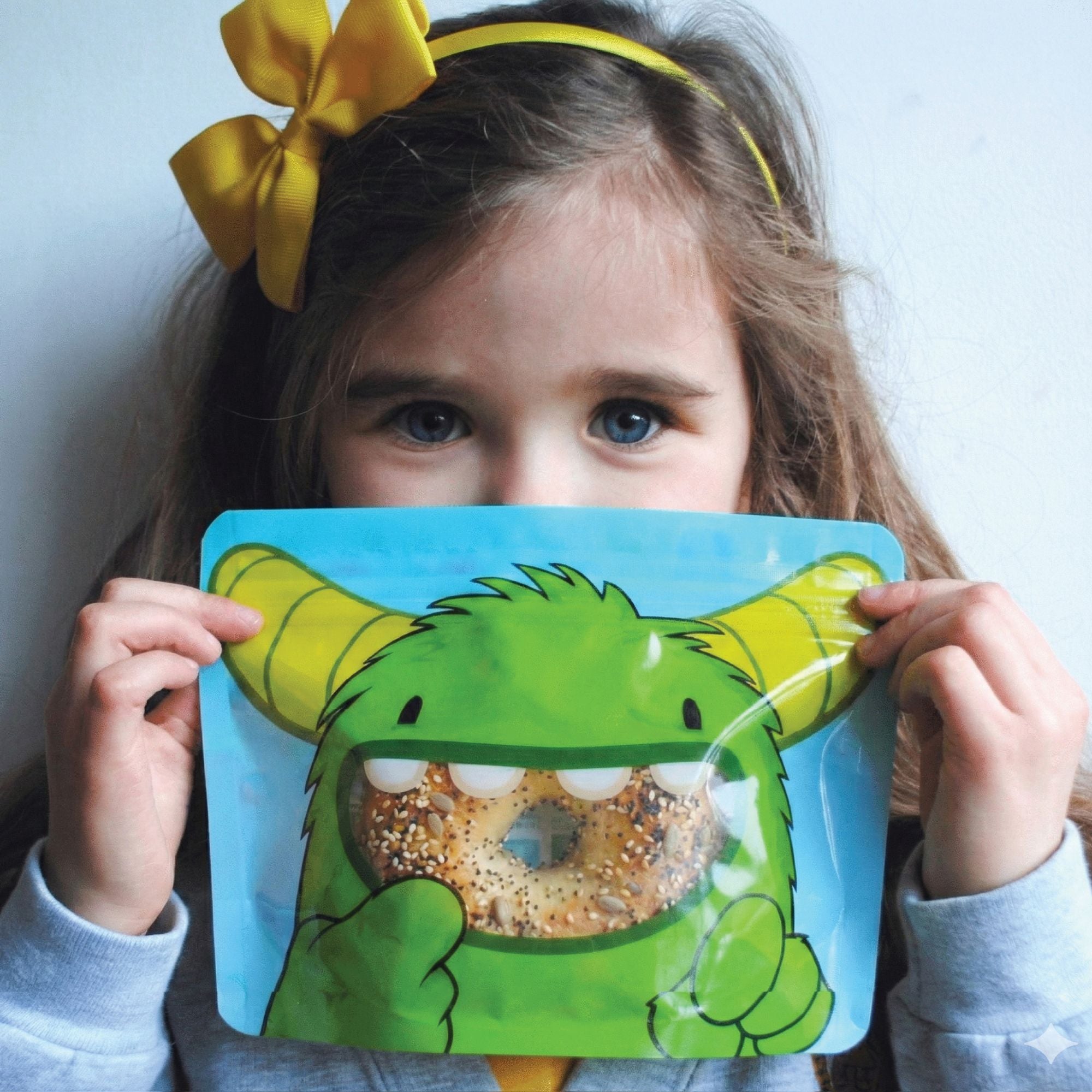 reception age school girl holding a monster bag filled with a seeded bagel