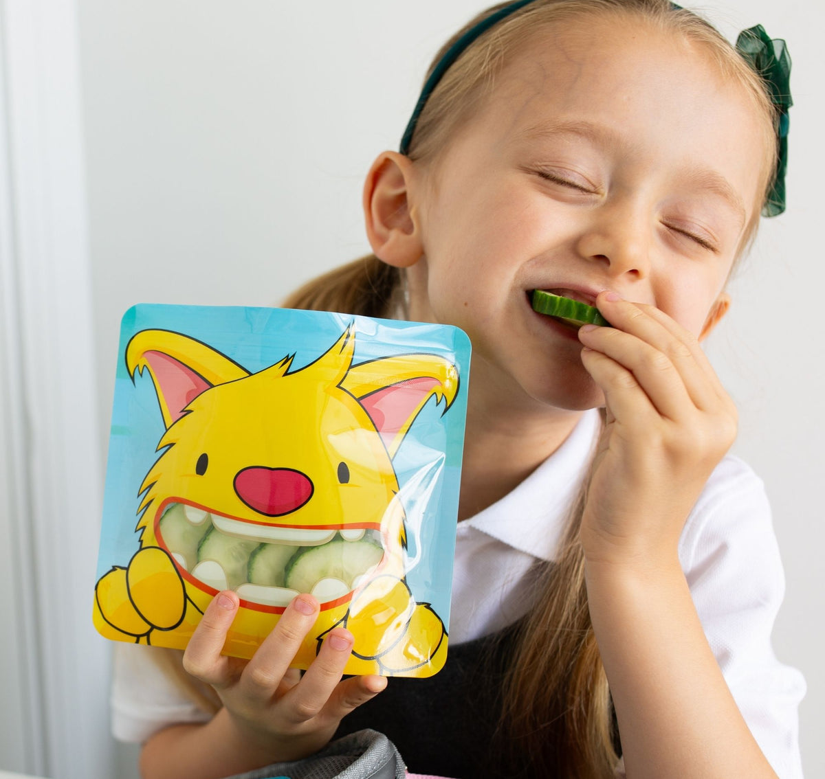 reception age school girl sat at lunch time eating cucumber from a yellow monster snack bag