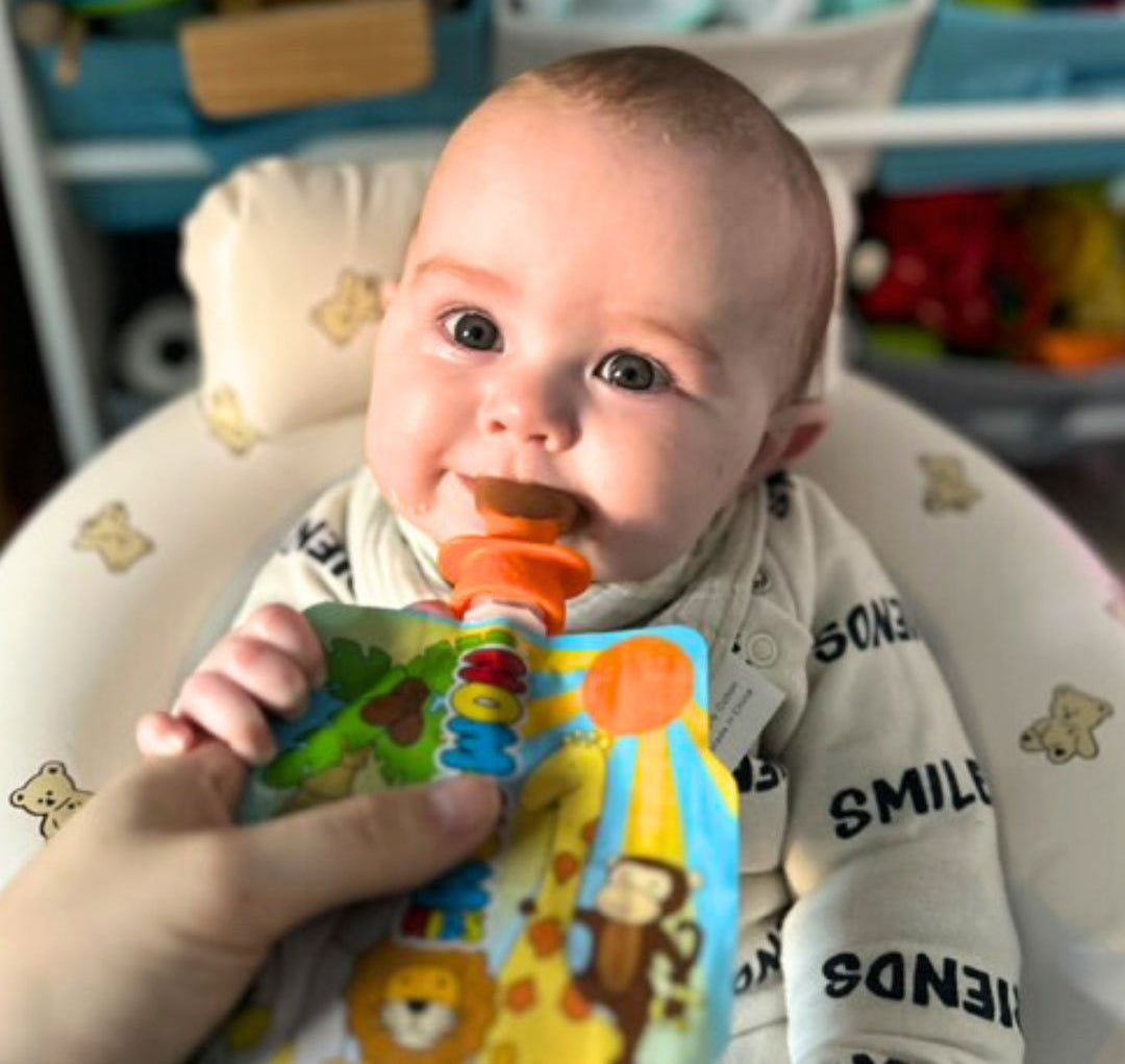 a weaning baby eating baby food from a Nom Nom Kids reusable food pouch with a silicone pouch spoon attached.