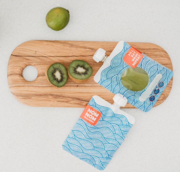 Green smoothie in a large capacity reusable pouch from the Nom Nom Kids wave range for older children, teens and adults. The pouches are on a chopping board with a kiwi and lime.