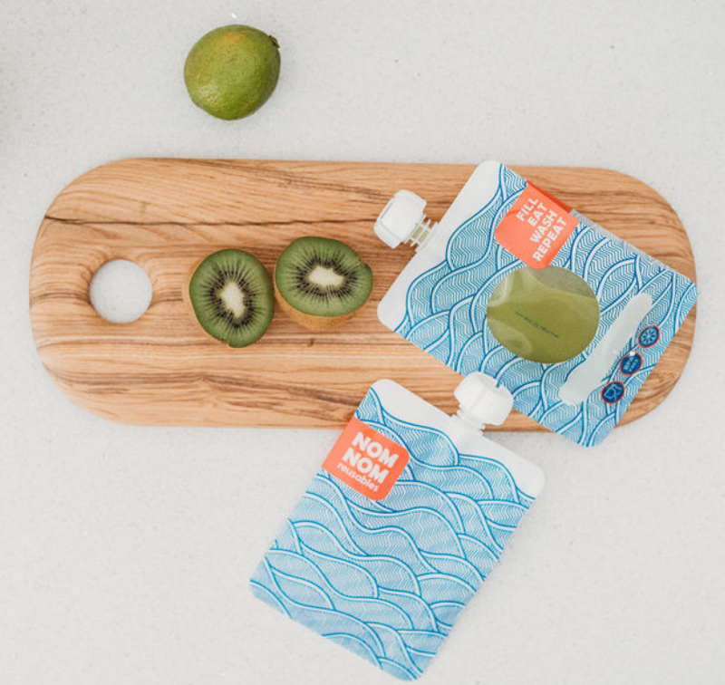 Green smoothie in a large capacity reusable pouch from the Nom Nom Kids wave range for older children, teens and adults. The pouches are on a chopping board with a kiwi and lime.