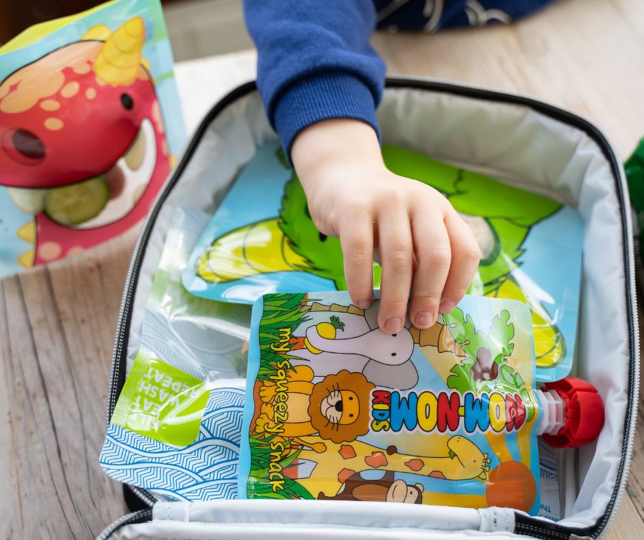 pre-schooler picking up a reusable pouch of yoghurt from his packed lunch at nursery