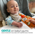 a baby sat in a high chair about to feed from a pouch of baby food using a Nom Nom Kids silicone pouch spoon