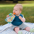 baby outdoors eating from reusable food pouch with silicone pouch spoon attached. 
