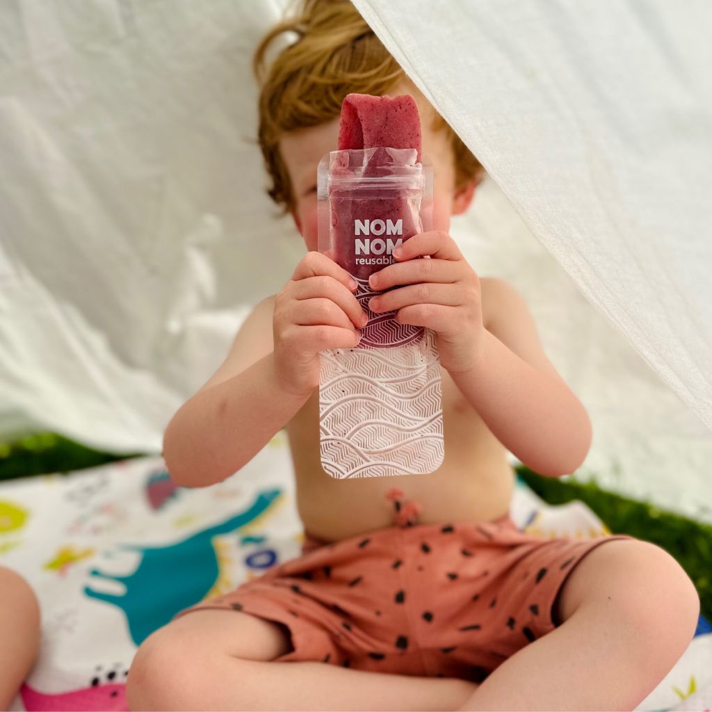 a child holding the Nom Nom kids reusable ice pop bag filled with a homemade ice pop filling 