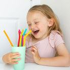 child holding a cup of Nom Nom kids reusable silicone straws 