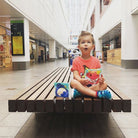 Child sat on a bench eating from a Nom Nom kids reusable snack bag 