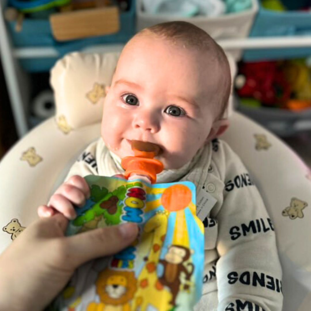 a weaning baby eating baby food from a Nom Nom Kids reusable food pouch with a silicone pouch spoon attached.